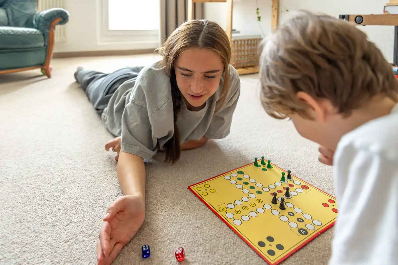 Girl playing a board game with her younger brother on the floor at home