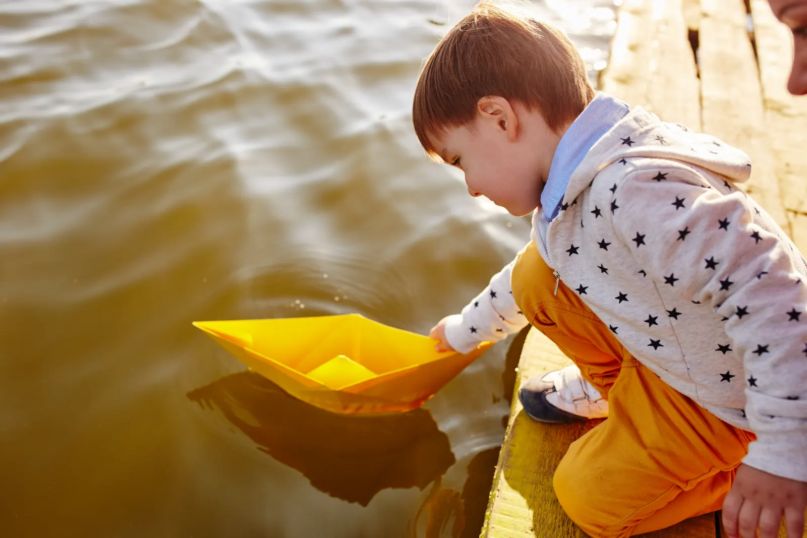 Boy floating a paper boat on the water