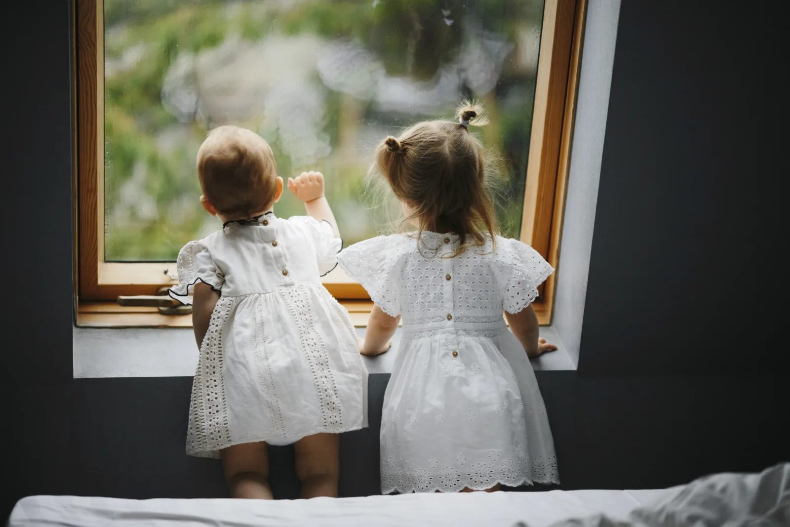 Two young children looking out of a window on a rainy day at home