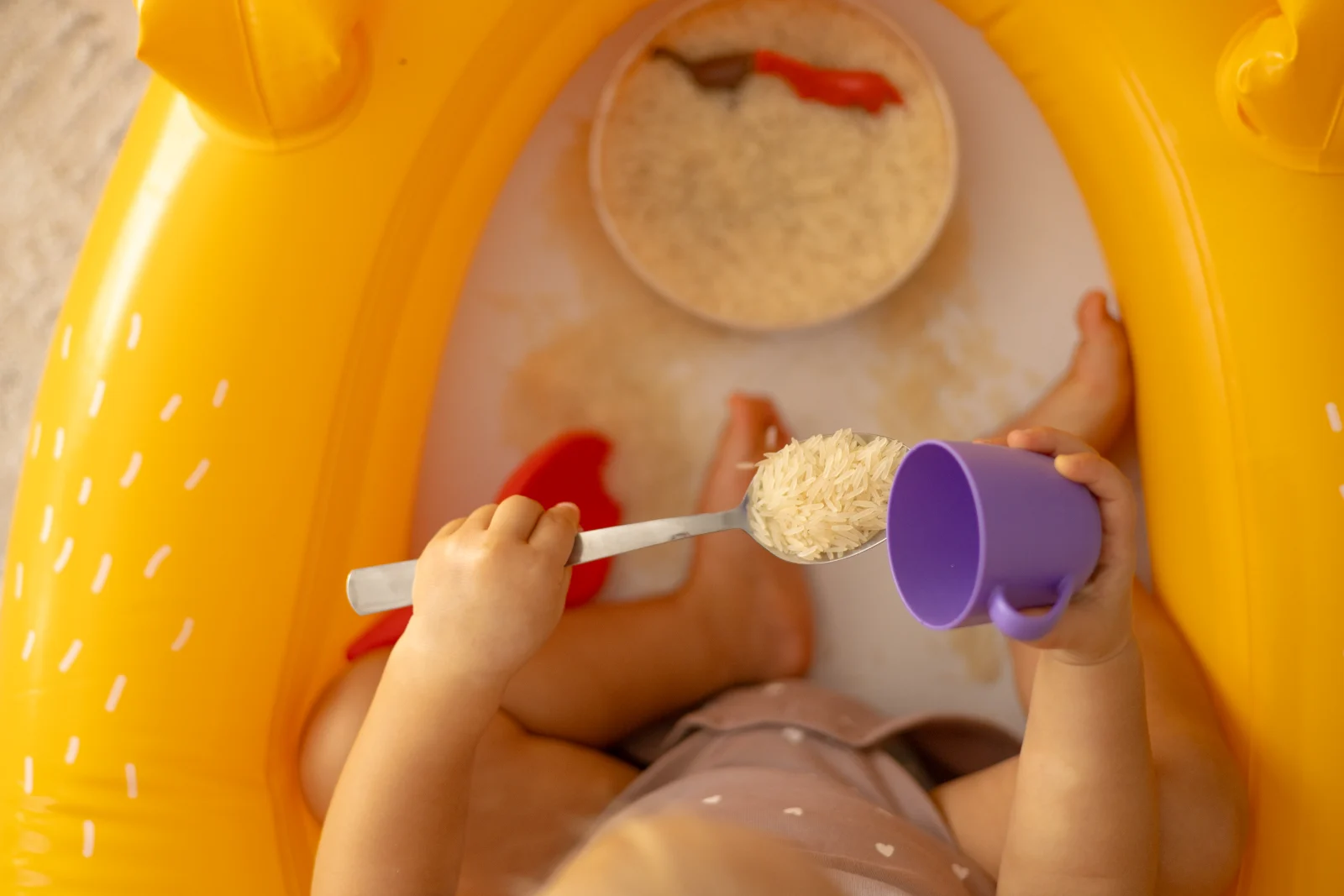 Toddler playing with rice and a spoon in a sensory bin